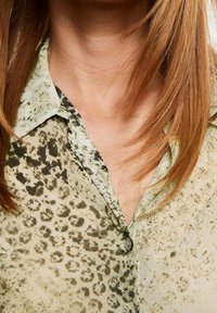 Blusa a maniche corte con motivo in un verde chiaro, caratterizzata da una sottile stampa leopardata, colletto e chiusura con bottoni. Tessuto testurizzato.