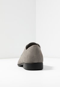 Šedá semišová bota s kulatou špičkou, nízkým černým podpatkem a hladkým povrchem, která se vyznačuje minimalistickým designem bez viditelných vzorů nebo akcentů.