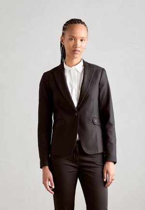 Black tailored blazer with notched lapels, two front pockets, and a single button closure, paired with a white collared shirt and dark trousers.