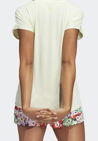 Jasnozielona, krótko rękawowa koszulka sportowa o gładkiej fakturze, połączona z szortami w kwiatowy wzór w odcieniach czerwieni, różu i zieleni.