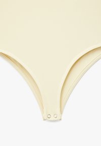 Lys gul bodysuit med en glat overflade, lavt skårne benåbninger og metalsnapper ved skridtet for nem påklædning.