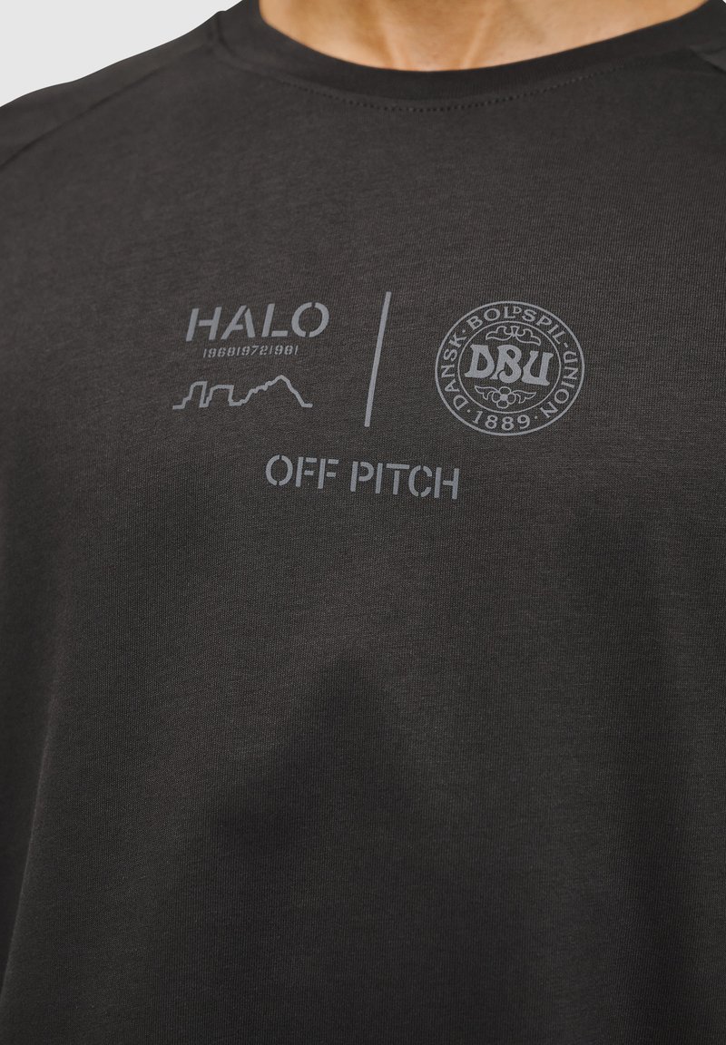 Czarna koszulka z miękkiego materiału z szarymi nadrukami, w tym tekstem "HALO" i "OFF PITCH", oraz okrągłym logo DBU.