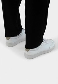 Weiße Sneaker mit einer glatten Oberfläche, die graue Akzente an der Ferse und ein einfaches Schnürdesign aufweisen, kombiniert mit schwarzen Hosen.