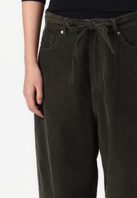 Olijfgroene ribfluwelen broek met een gestructureerd oppervlak, voorzien van een strikceintuur in de taille en zijzakken.