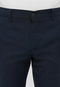 Marineblaue Hose aus strukturiertem Stoff; mit Knopfverschluss, Gürtelschlaufen und einem schlichten Design ohne sichtbare Taschen.