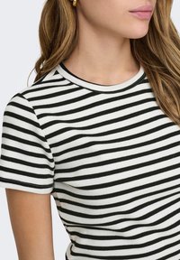 T-shirt à rayures blanches et noires avec une texture côtelée, col rond et manches courtes. Détails de couture visibles le long du col et de l'ourlet.