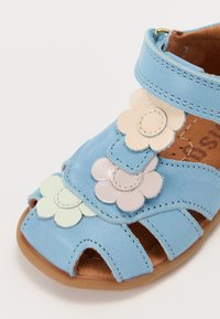 Blå lær sandaler med blomsterdetaljer i pastellfarger, åpen tå-design, justerbar stropp og tan interiør med sømdetaljer.
