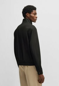 Schwarze Bomberjacke mit hohem Kragen, elastischem Saum und Bündchen. Glatte Textur mit minimalistischem Design und ohne sichtbare Muster.