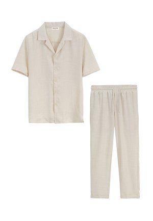 Chemise beige à manches courtes avec boutons et col, et pantalon beige assorti à cordon, posés à plat sur un fond blanc.
