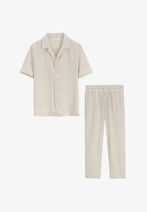 Chemise beige à manches courtes avec boutons et col, et pantalon beige assorti à cordon, posés à plat sur un fond blanc.
