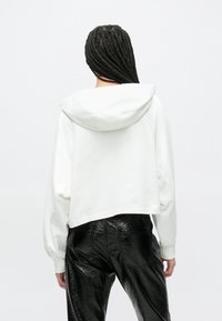 Balta īsi griezta kapuce ar kapuci un pūkainām piedurknēm. Kombinēts ar spīdīgām melnām mākslīgās ādas biksēm. Minimālistisks dizains, gluda tekstūra.