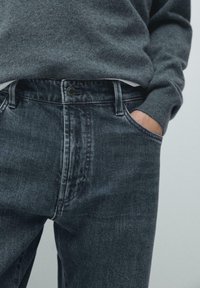 Ciemne dżinsy z klasycznym krojem, z zamkiem błyskawicznym i zapięciem na guzik, kieszeniami bocznymi oraz lekko przetartym wykończeniem. W zestawie z szarym swetrem.