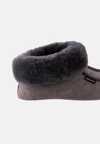Grå ruskindsko med en fuzzy sort shearling-manchet, rund form og et logomerke på siden, designet til komfort og varme.