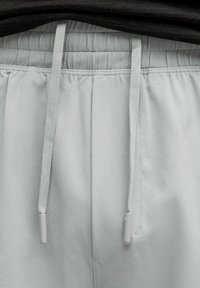 Šviesiai pilki sportiniai džinsai su elastingu liemeniu, raišteliais ir lygiu paviršiumi. Pabaigoje raištelių yra pilki metaliniai aksesuarai.