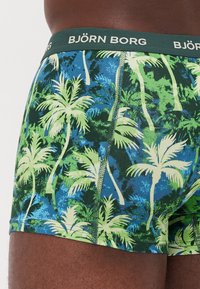 Grün und blau gemusterte Boxershorts mit Palmenblättern, ausgestattet mit einem grünen elastischen Bund, der mit "BJÖRN BORG" beschriftet ist, und einem figurbetonten Design.