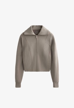Strihaná bundová mikina na zips v mäkkej béžovej látke s vysokým golierom a rebrovanou textúrou. Obsahuje detaily predného švu a priliehavé manžety.