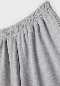 Graue elastische Hose mit gerafftem Stoff, der eine weiche Textur und ein entspanntes Design mit Falten für zusätzlichen Volumen zeigt.