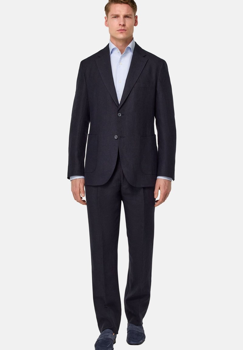 Costume bleu marine foncé avec deux boutons, revers crantés et deux poches avant. Assorti à une chemise rayée bleu clair et à des mocassins navy.