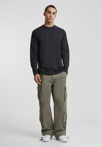 Svart langermet skjorte og olivengrønne cargo-bukser med lommer. Hvite sneakers. Løs passform, strukturert design og lett teksturdetalj på stoffet.
