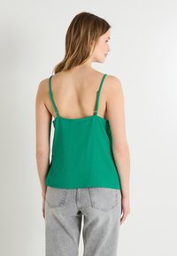 Top verde sin mangas con tirantes finos, de corte relajado, hecho de una tela ligera. La vista posterior muestra una textura suave y detalles de diseño mínimos.