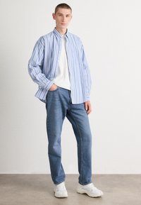 Modra in bela črtasta srajca z gumbi čez belo majico, v kombinaciji z modrimi jeans hlačami in belimi supergami. Priložnostna obleka, lahka tekstura materiala.