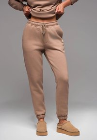 Beige Jogginghosen mit elastischem Bund, Kordelzug und gerippten Bündchen, kombiniert mit tanfarbenen Slipschuhen.