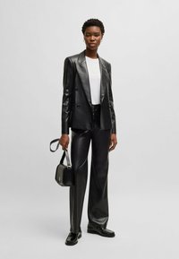 Blazer doppiopetto in eco-pelle nera e pantaloni abbinati, abbinati a una t-shirt bianca, borsa nera e scarpe lucide nere.