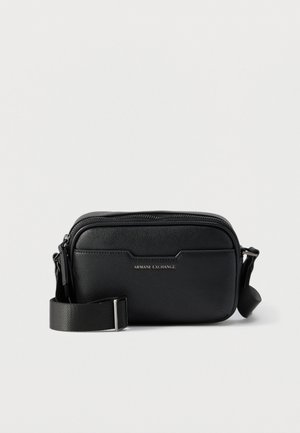 Sac bandoulière en cuir noir Armani Exchange avec poche frontale, fermeture éclair argentée et bandoulière en tissu ajustable sur un fond uni.