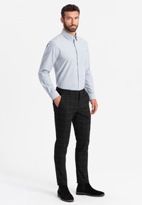 Camisa de botones azul claro con un bolsillo, combinada con pantalones de cuadros negros y botines de ante negros. Tejido suave y corte a medida.