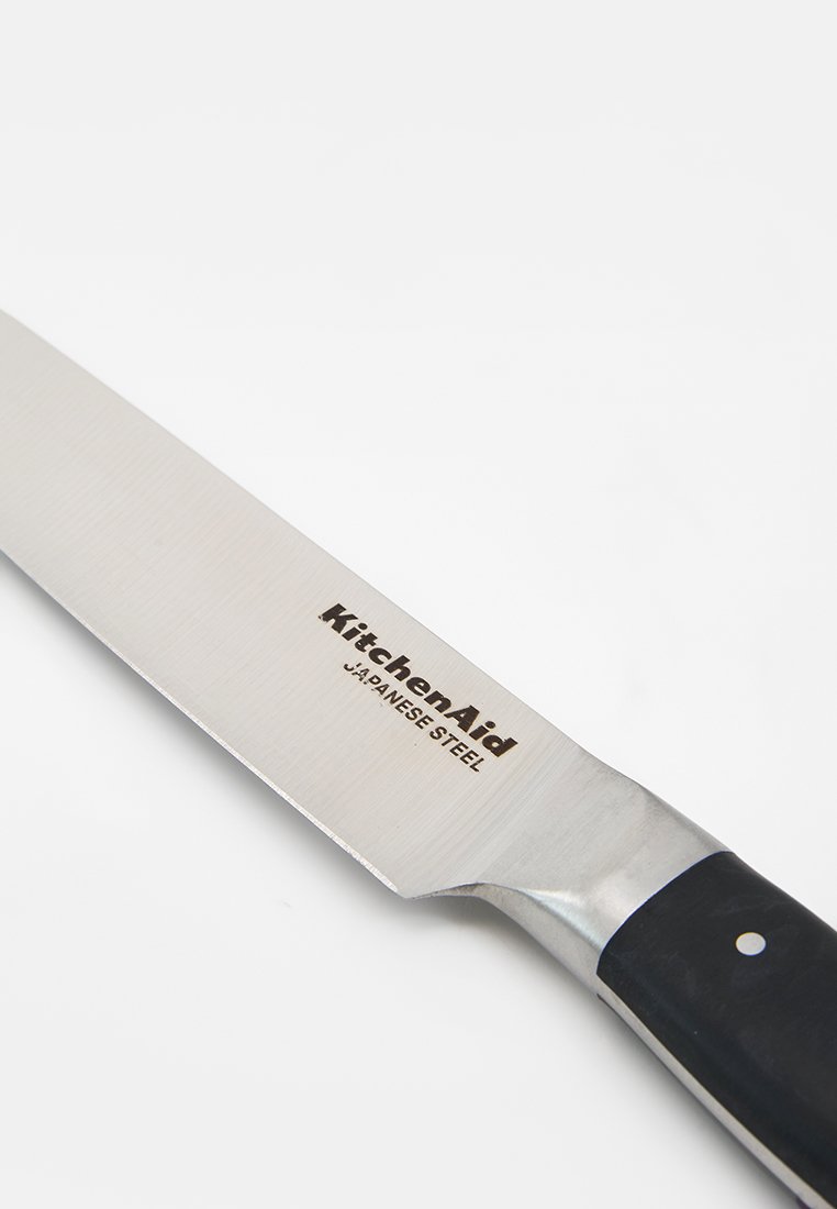 Lame dentelée en acier japonais KitchenAid avec manche noir sur une surface blanche, gros plan en angle du couteau.