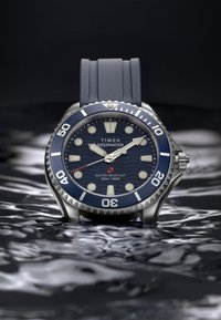 Zegarek Timex Deepwater z niebieską tarczą, stalową obudową ze stali nierdzewnej, gumowym paskiem, świecącymi znacznikami i jednokierunkową bezelą. Wodoszczelny do 200m.
