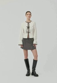 White blouse with black ribbon tie, long sleeves; grey pinstriped mini skirt; black knee-high boots. Simple, structured design.