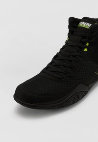 Black high-top sneaker featuring mesh and synthetic materials, lace-up design, textured sole, and neon accents for visibility.