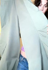 Personne tenant un pantalon vert clair, visage partiellement visible avec des cheveux bouclés, portant un jean bleu et un haut violet en dessous.