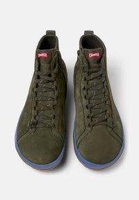 Zapatillas altas verdes con suelas azules y cordones grises, con el logo de la marca "Camper" en etiquetas rojas en la lengüeta.