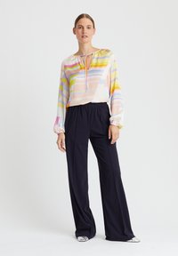 Leichte, mehrfarbige Bluse mit Streifen und einem Schlitzkragen, kombiniert mit dunklen, weiten Hosen. Glattes Material mit elastischen Bündchen.