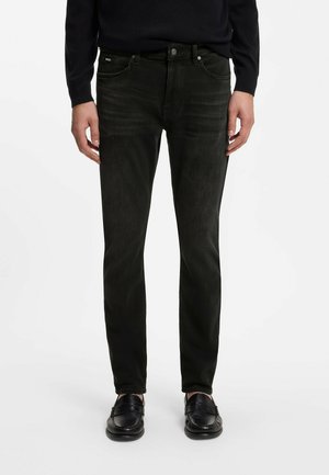 Homme portant un jean slim noir et des mocassins en cuir noirs, debout devant un fond blanc.