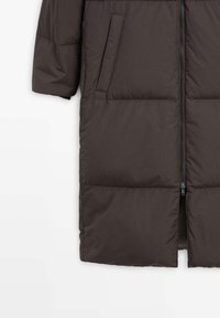 Cappotto lungo imbottito marrone con tasche laterali e zip frontale, parzialmente visibile su uno sfondo bianco.
