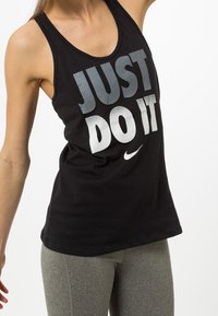 Camiseta sin mangas negra con el texto "JUST DO IT" en letras grandes de color gris y blanco, con un cuello redondo y un logotipo de Nike en la parte inferior.