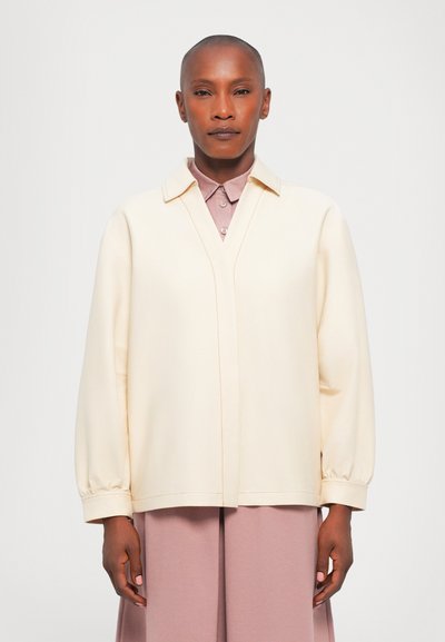 Crème-kleurige blouse met lange mouwen en een V-hals, voorzien van een gestructureerde kraag, elastische manchetten en contrasterende stikdetails.