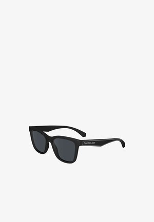 Lunettes de soleil rectangulaires noires avec verres foncés et logo "Calvin Klein Jeans" sur les branches, légèrement inclinées vers la droite.