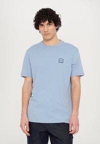Tricou din bumbac de culoare albastru deschis, cu mâneci scurte, decolteu rotund și un mic patch rectangular cu logo pe piept. Croială lejeră și textură netedă.
