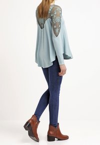 Světle modrý top s vyšívanými průhlednými rukávy, asymetrickým lemem, spojený s tmavě modrými skinny džíny a hnědými kotníkovými botami.