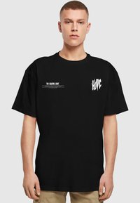Sort bomulds T-shirt med korte ærmer, rund hals, for-tekst "THE GUIDING LIGHT," og "HOPE" i en stiliseret hvid skrifttype på brystet.