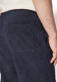 Marineblaue Cordhosen mit sichtbarer Gesäßtasche, die eine vertikale Rippstruktur aufweisen und über einen elastischen Bund für zusätzlichen Komfort verfügen.