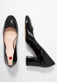 Czarne lakierowane szpilki z okrągłym noskiem i kwadratowym obcasem, z małym czerwonym akcentem przy podstawie wewnątrz. Gładka tekstura.
