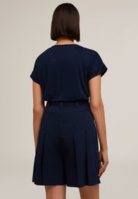 Top scurt de culoare bleumarin cu mansete răsucite și o croială lejeră, asortat cu pantaloni scurți bleumarin plisati, având talie cu curea și o textură netedă.