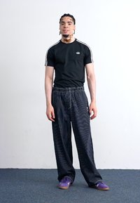 Zwart T-shirt met korte mouwen en witte strepen, gecombineerd met loszittende gestreepte broek. De outfit heeft paarse schoenen en is relaxed fit.