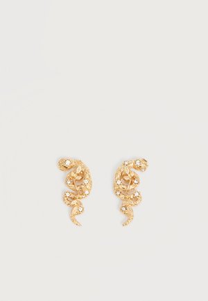 Pendientes en forma de serpiente con tono dorado adornados con pequeños cristales claros sobre un fondo claro liso.