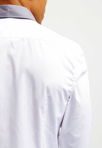 Camicia bianca con colletto grigio, caratterizzata da una texture liscia e una vestibilità su misura. Le cuciture visibili lungo le cuciture valorizzano il design.